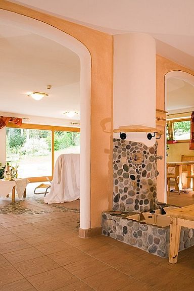 Cozy room with wooden furniture and stone fireplace near Wilder Kaiser, featuring large windows with lush views, creating a warm and inviting atmosphere.