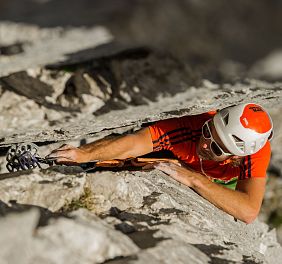 A climber scales a rocky cliff in the Wilder Kaiser, wearing safety gear and a helmet, emphasizing the adventurous spirit and rugged landscape of the region.