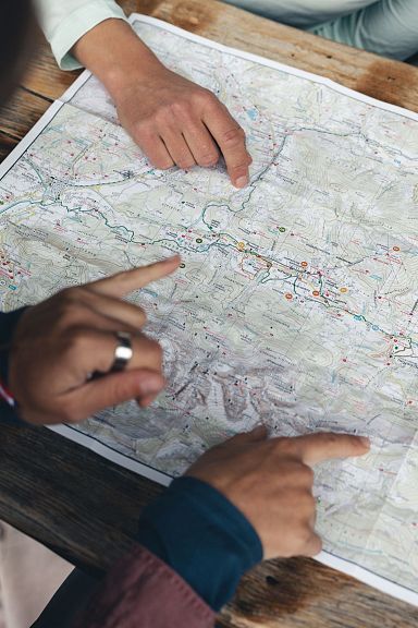 A close-up of hands pointing at a detailed map, planning a hike in the picturesque Wilder Kaiser region, known for its majestic mountains and outdoor activities.
