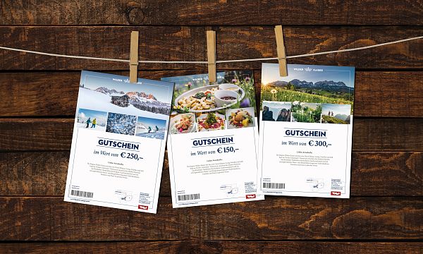 Three gift vouchers hanging on a wooden background, each secured with a clothespin. The vouchers display scenic images and monetary values.