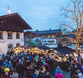 Menschen genießen einen stimmungsvollen Weihnachtsmarkt mit beleuchteten Ständen und festlich geschmücktem Baum, umgeben von traditionellen Tiroler Gebäuden.