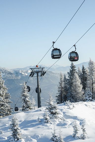 Snowy landscape of Wilder Kaiser with ski lift and frosted pines, highlighting winter sports. Blue sky enhances the majestic mountain view.