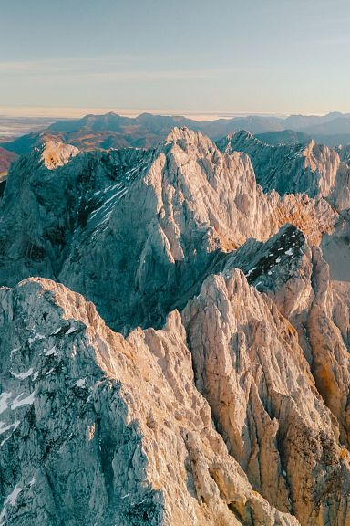 Luftaufnahme der beeindruckenden Felsen und Gipfel des Wilder Kaiser Massivs in Tirol, umgeben von malerischen Tälern unter einem klaren, blauen Himmel.