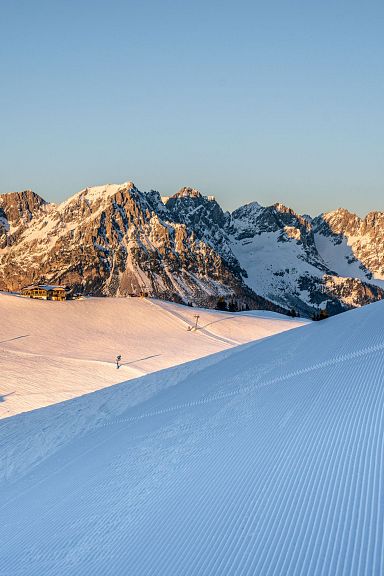 Schneebedeckte Berge im Abendlicht mit Skispuren. Klare blaue Himmel und Wälder im Hintergrund. Eine idyllische Winterlandschaft in den Alpen.
