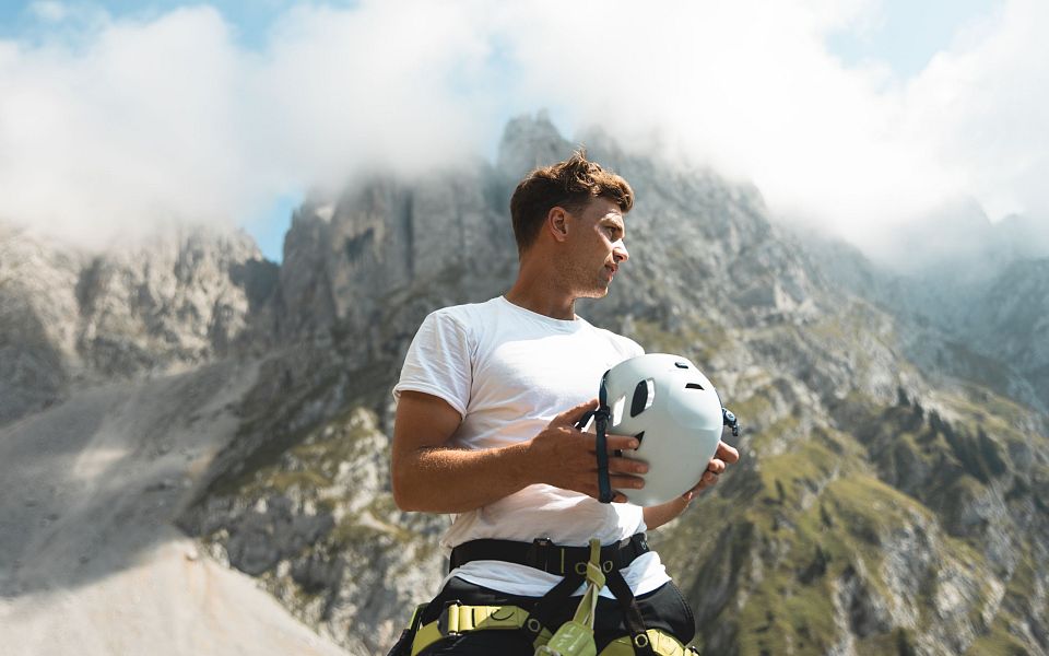 A man with climbing gear in front of the misty peaks of the Wilder Kaiser mountains, showcasing an adventurous setting surrounded by nature's beauty.