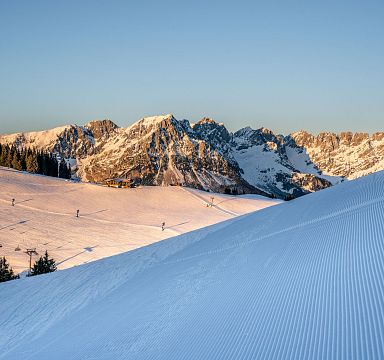 Schneebedeckte Berge im Abendlicht mit Skispuren. Klare blaue Himmel und Wälder im Hintergrund. Eine idyllische Winterlandschaft in den Alpen.