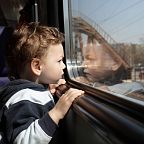 Ein Kind schaut aus einem Zugfenster, die Landschaft und Brückenkonstruktionen spiegeln sich im Glas. Es trägt eine gestreifte Kapuzenjacke.