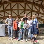 Eine Gruppe von sieben Personen posiert lächelnd unter einer holzverkleideten Kuppel im Freien. Im Vordergrund sind Pflanzen zu sehen.