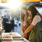 Zwei Frauen in traditionellen Trachten betrachten Schmuck an einem Marktstand im Freien bei Sonnenuntergang. Die Szene wirkt lebhaft und gemütlich.