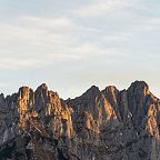 Sonnenuntergang über einem felsigen, gezackten Gebirgsmassiv mit dramatischem Licht und Schatten. Der Himmel ist leicht bewölkt und die Felsen leuchten golden.