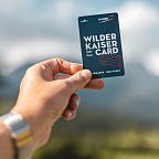 A hand holding a card labeled 'Wilder Kaiser Card' against a blurred mountainous background.