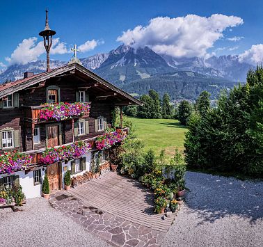 Aufnahme eines Bauernhauses mit Blumenschmuck und Bergen im Hintergrund