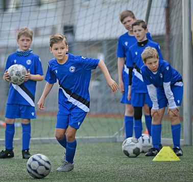 Kind läuft zum Fußball, im Hintergrund schauen 4 weitere Kinder gespannt zu