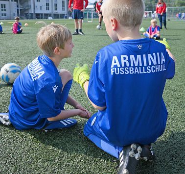 Zwei Kinder in blauem Fußballdress knien am Fußballplatz