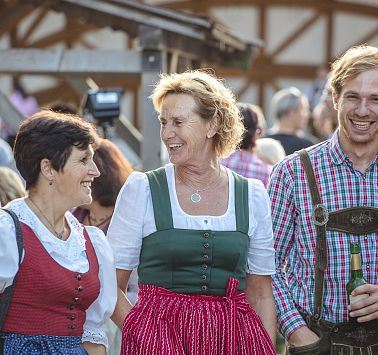 Drei Personen in Tracht gekleidet stehen nebeneinander und lachen zusammen