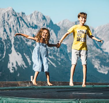 Kinder springen auf Trampolin vor Bergpanorama