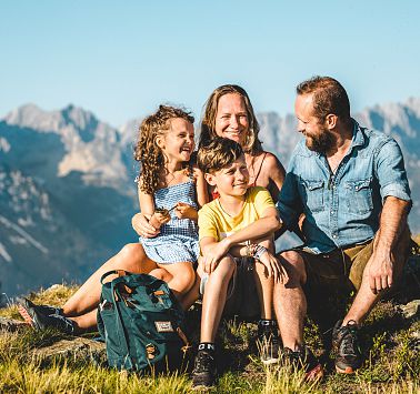 Familie sitzt auf Almwiese und unterhält sich miteinander