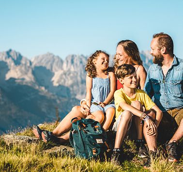 Familie sitzt auf Almwiese und unterhält sich miteinander