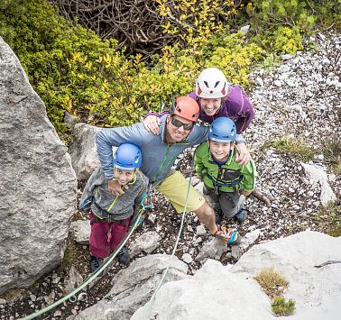 Eine vierköpfige Familie in Kletter-Ausrüstung blickt der Felswand hoch.