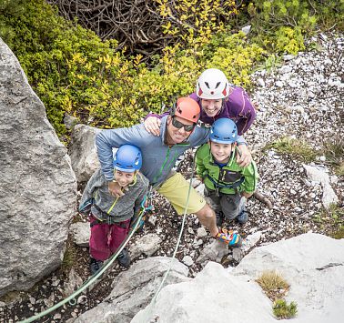 Eine vierköpfige Familie in Kletter-Ausrüstung blickt der Felswand hoch.