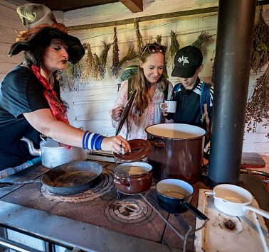 Hexe steht in uriger Küche und kocht mit alten Töpfen