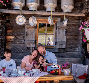 Familie sitzt an gedecktem Tisch vor uriger Almhütte