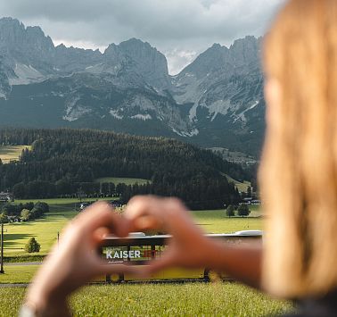 Frau formt mit Händen ein Herz und zeigt auf Bus