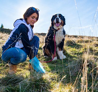 Frau benutzt Gassi-Sackerl und Hund sitzt neben ihr