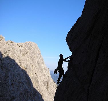 Ein Kletter steht im Schatten der vor sich liegenden Felswand.